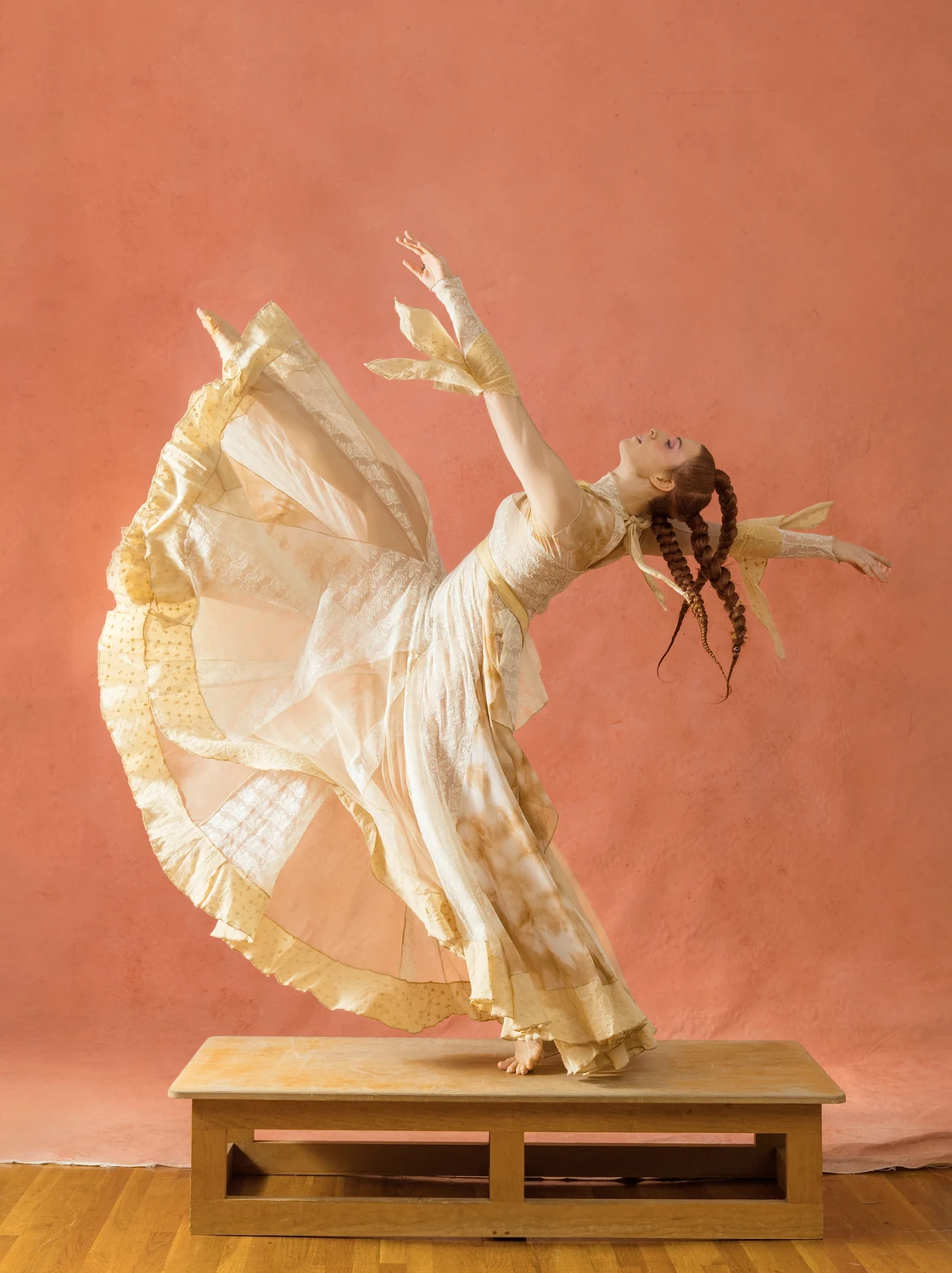 Performer arching backward as a cream skirt lifts into a wide sculptural curve.