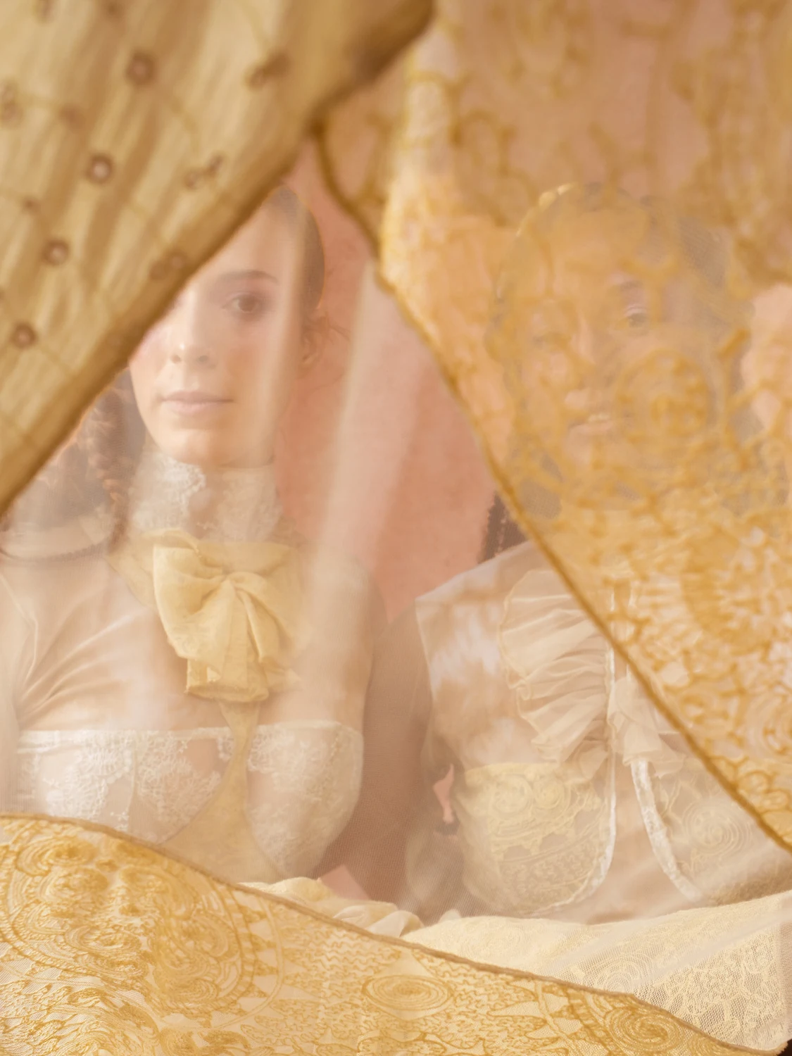 A performer seen through translucent patterned cream fabric against a terracotta set.