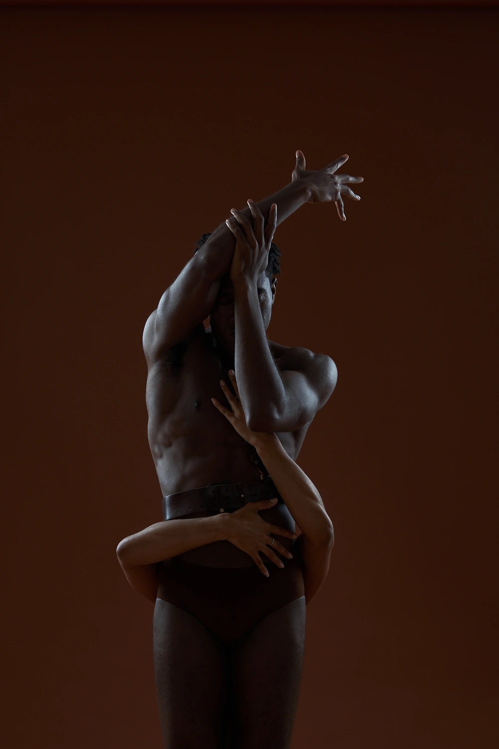 Two people intertwined in a vertical dark silhouette with arms reaching upward.