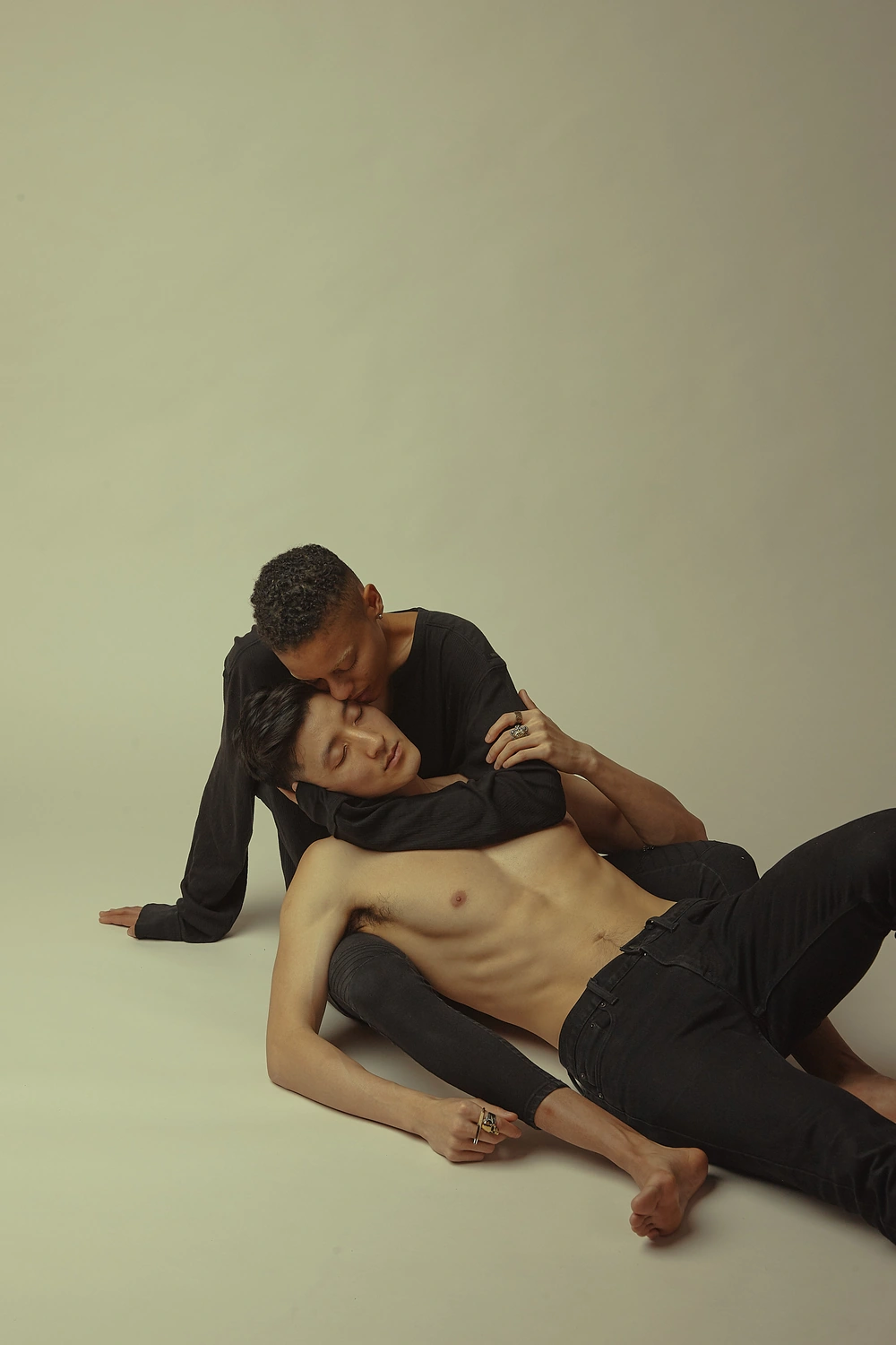 Two people reclining together on the studio floor with one figure supporting the other.