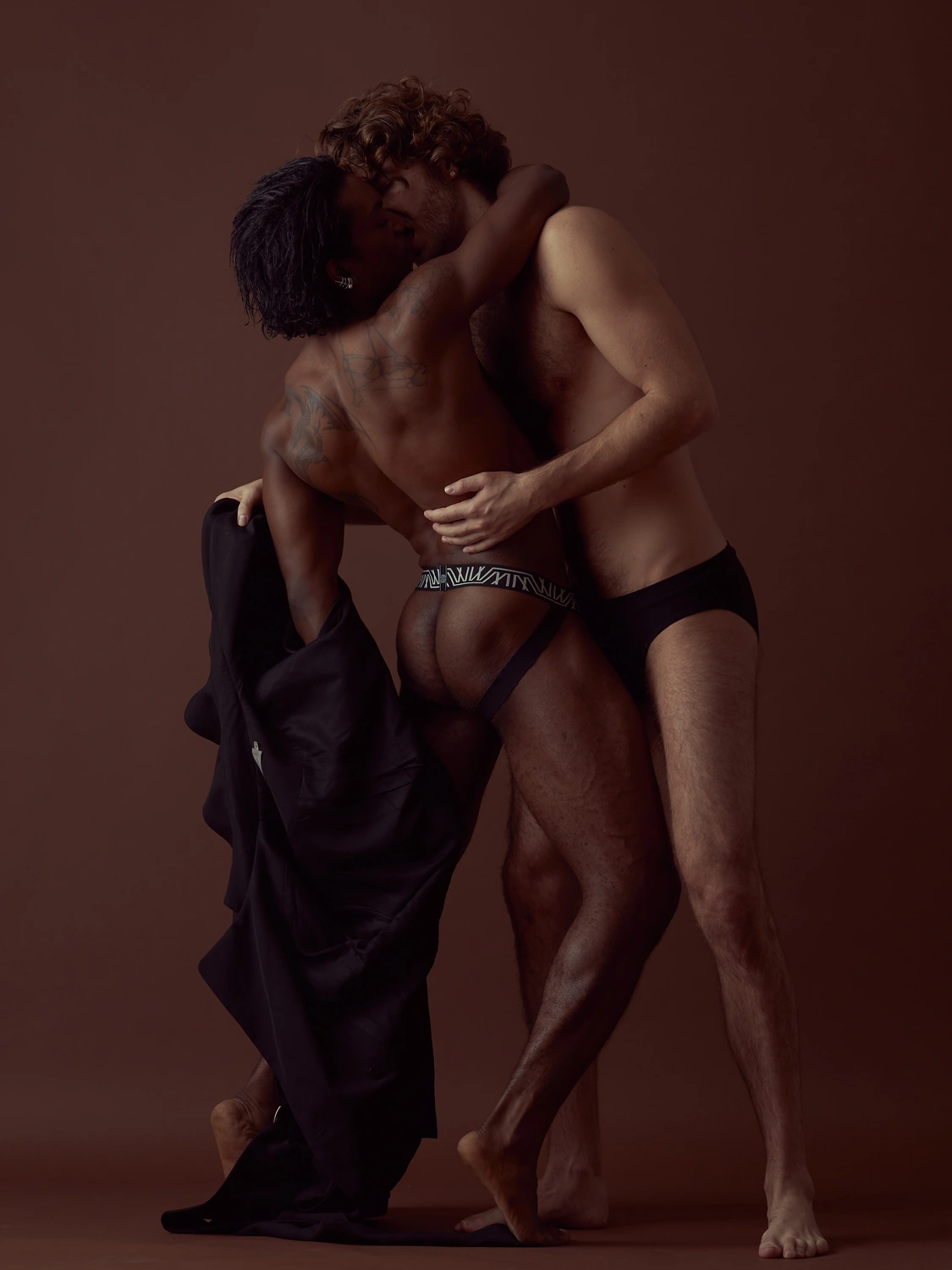 Two people standing closely together with dark fabric gathered around their bodies.