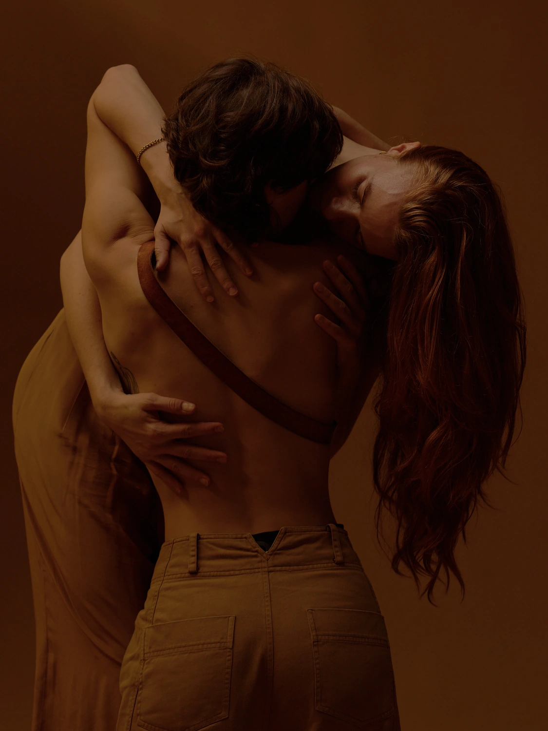 Two people standing in a close embrace under warm brown light.