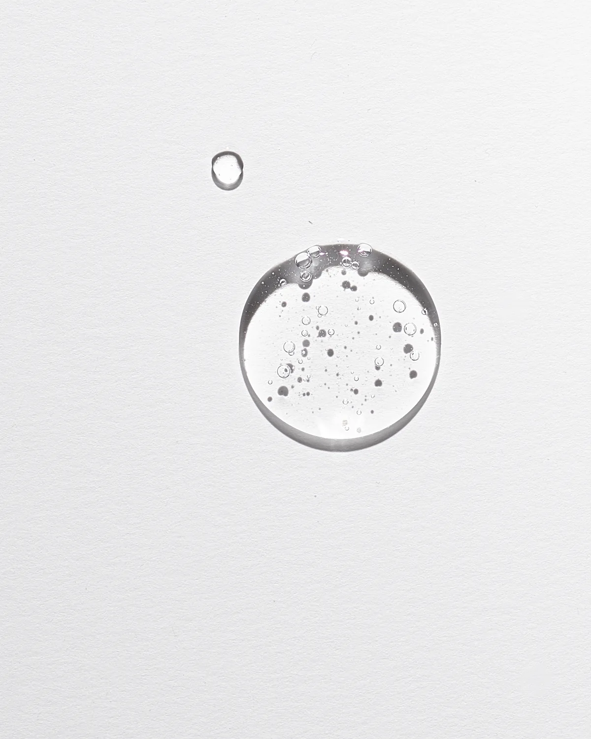 Clear serum droplets suspended on a white textured surface.