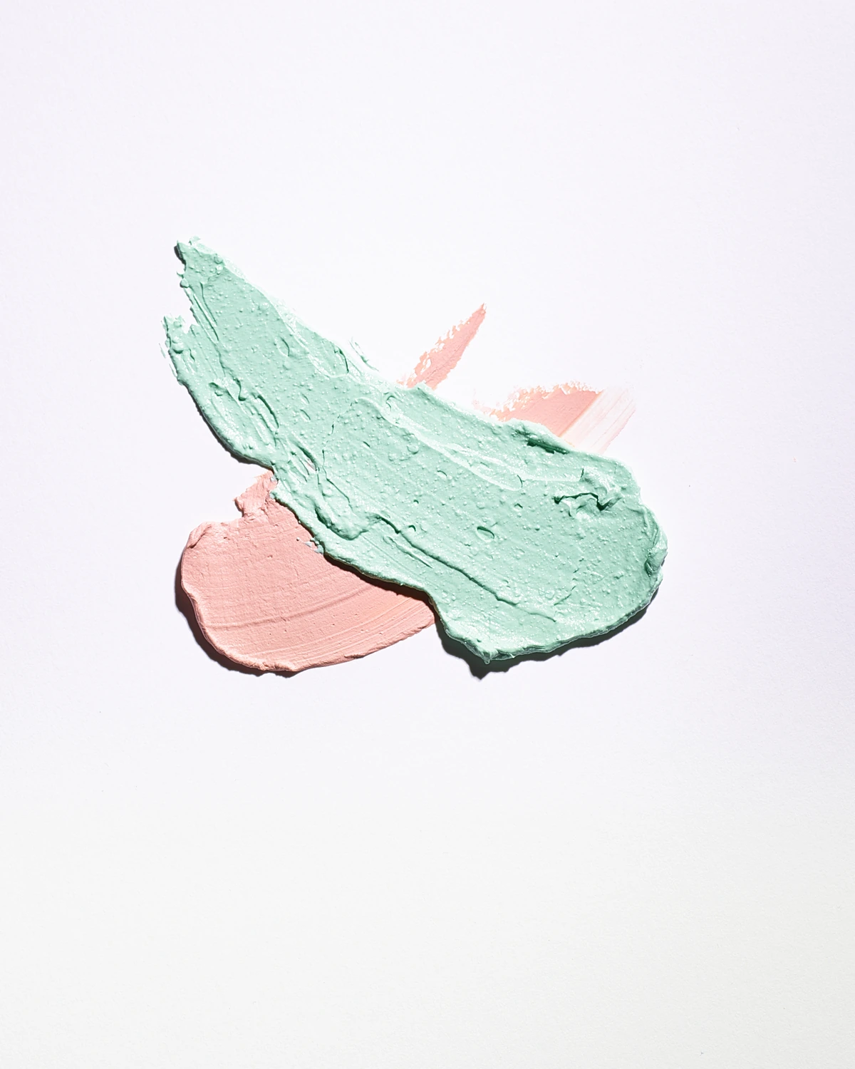 Mint green and pale pink cosmetic cream strokes on a white background.