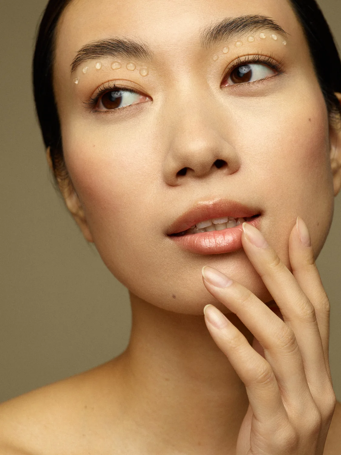 Dewy beauty portrait with luminous skin and fingertips resting near glossy lips.