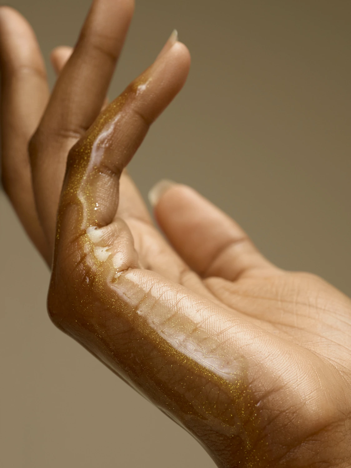 Golden skincare oil on a hand photographed as a reflective sculptural material