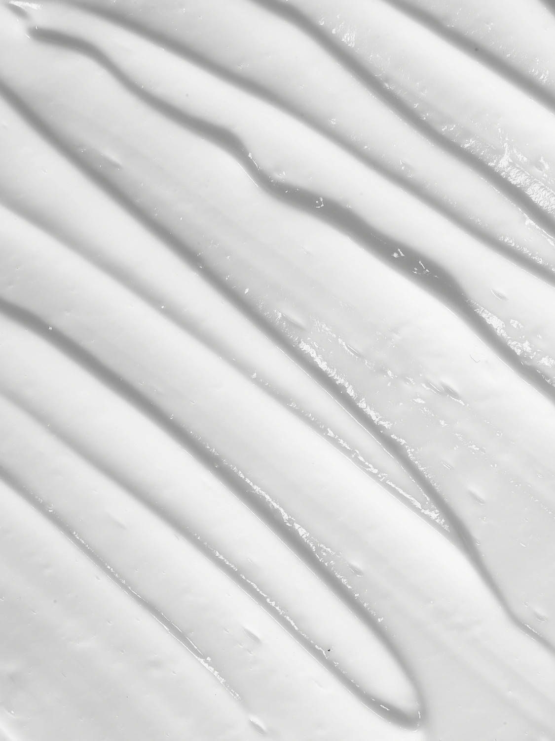 Transparent skincare serum drawn in a long streak across a white ribbed surface.