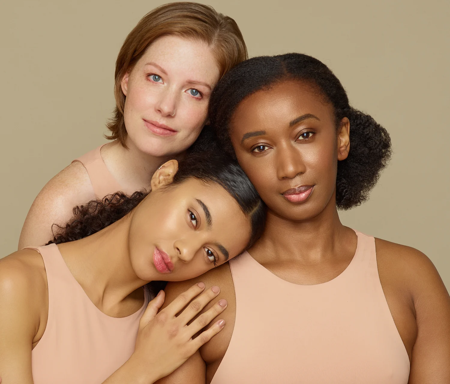 Three women with varied skin tones posed closely together in coordinated neutral beauty styling.