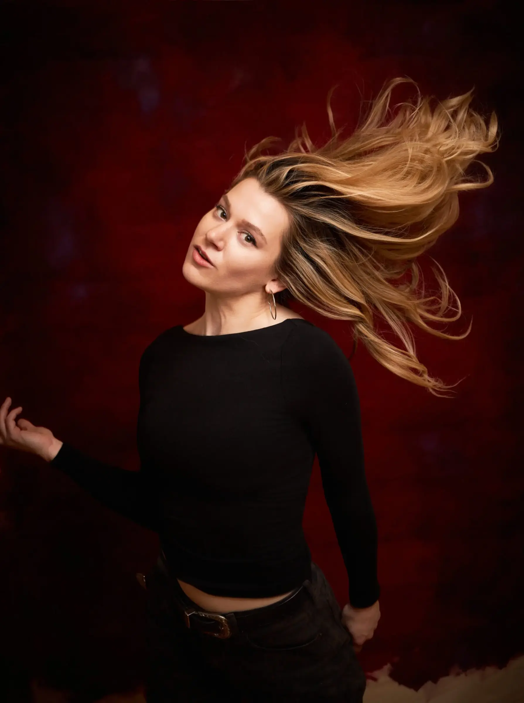 Portrait of a person in black against a deep red backdrop, with long hair sweeping dramatically across the frame.